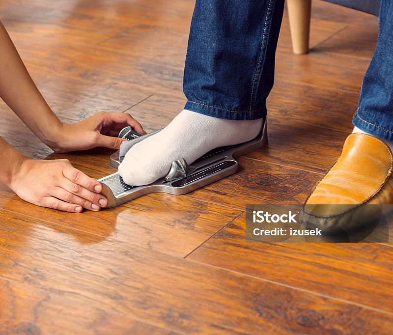 Shop assistant measuring customer's foot in shoe store. Focus on hands and feet.